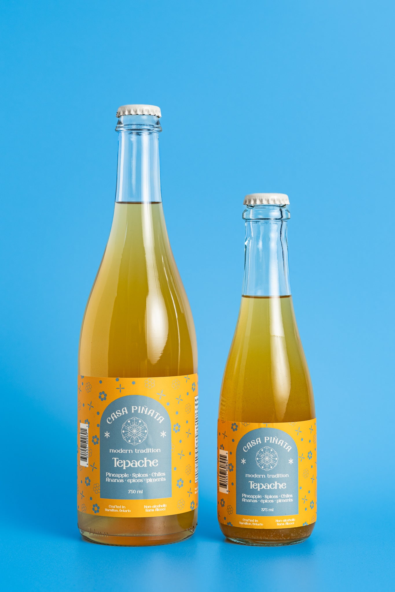 Two bottles of Casa Piñata Tepache Mocktail, one 375ml and one 750ml clear champagne bottle, against a blue background.