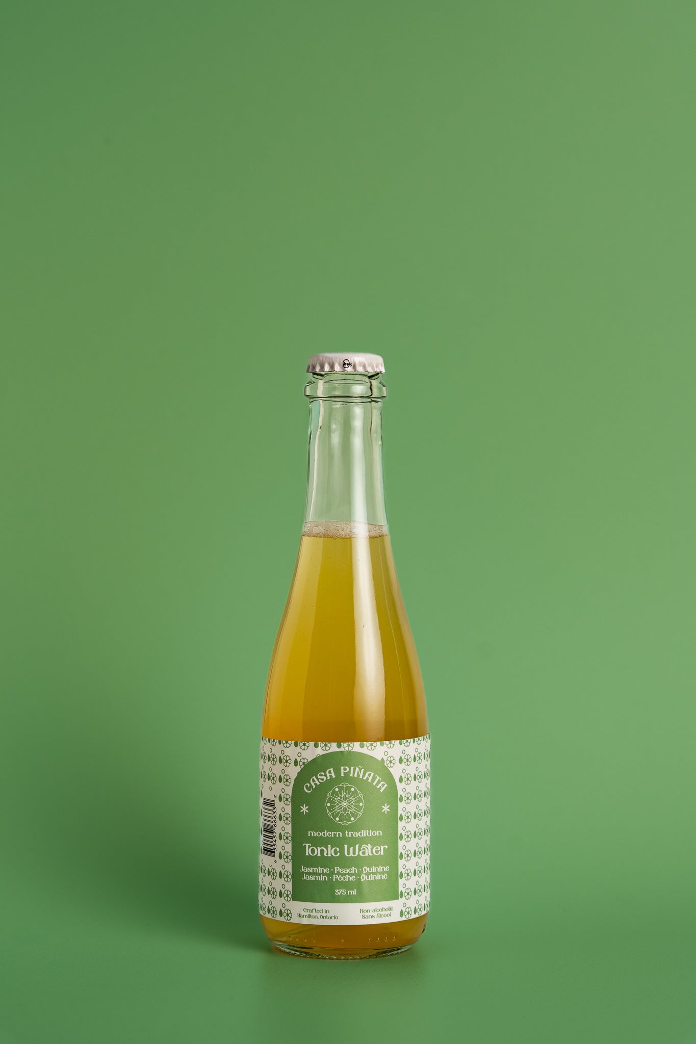 375ml clear champagne bottle of Casa Piñata tonic water with jasmine flowers against a green background